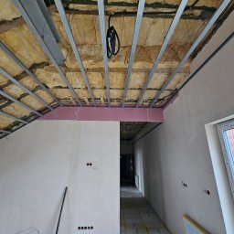 QMetters Sp. z o.o. - Poddasze w trakcie adaptacji: wełna mineralna między profilami sufitowymi, częściowo zamontowane płyty kartonowo-gipsowe, widoczne okno dachowe i instalacje elektryczne.