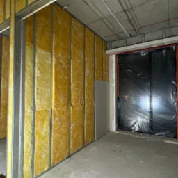 Wnętrze w trakcie prac wykończeniowych w Sosnowcu: widoczne metalowe profile konstrukcyjne, żółta wełna mineralna jako izolacja termiczna oraz częściowo zamontowane płyty gipsowo-kartonowe.