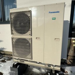 QMetters Sp. z o.o. - Zewnętrzna jednostka pompy ciepła Panasonic R32 zamontowana na betonowych blokach w zimowym otoczeniu, widoczne ślady na śniegu.