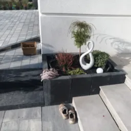 Ogr&oacute;dek z roślinami i rzeźbą w kształcie &oacute;semki, obok schod&oacute;w i kostki brukowej, z parą but&oacute;w na pierwszym planie.