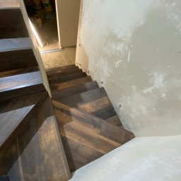 Saranda - montaż podłóg Rafał Trębski - Wnętrze w trakcie wykończenia ze schodami z ciemnego drewna ułożonymi w jodełkę, widoczne surowe ściany i instalacja elektryczna