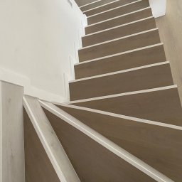 Saranda - montaż podłóg Rafał Trębski - Widok z góry na spiralne schody z drewnianymi stopniami i białymi listwami wykończeniowymi; na dolnym stopniu widoczne buty osoby fotografującej.