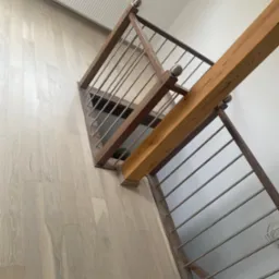 Jasna podłoga z desek i drewniane schody z metalowymi barierkami, widok z góry, oświetlenie dzienne. Minimalistyczny design z elementami naturalnego drewna.