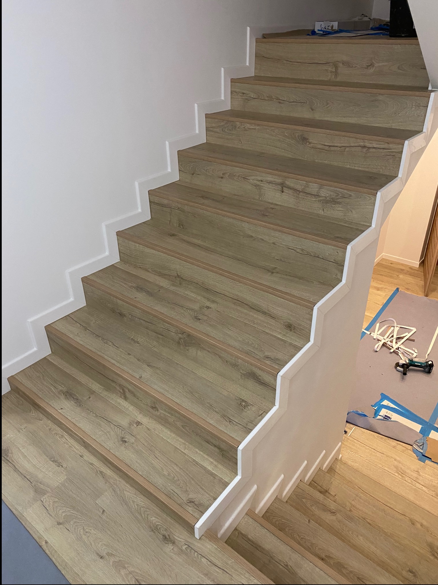 Schody wykończone panelami imitującymi drewno, z białymi listwami przypodłogowymi i zabezpieczonym podłożem na dole, widoczne narzędzia.