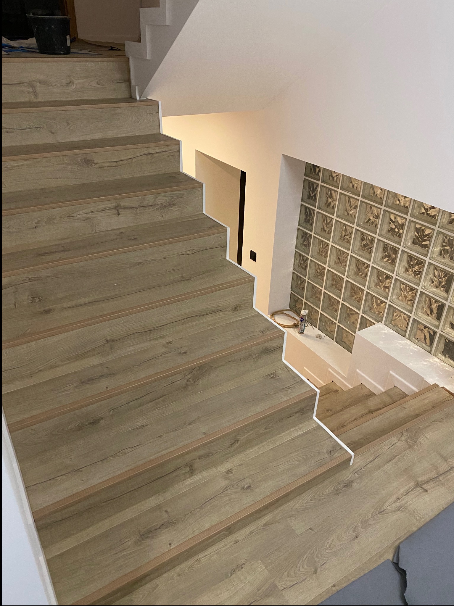 Schody wyłożone panelami imitującymi drewno, z białymi listwami wykończeniowymi, widok z góry, obok ściana z luksferami