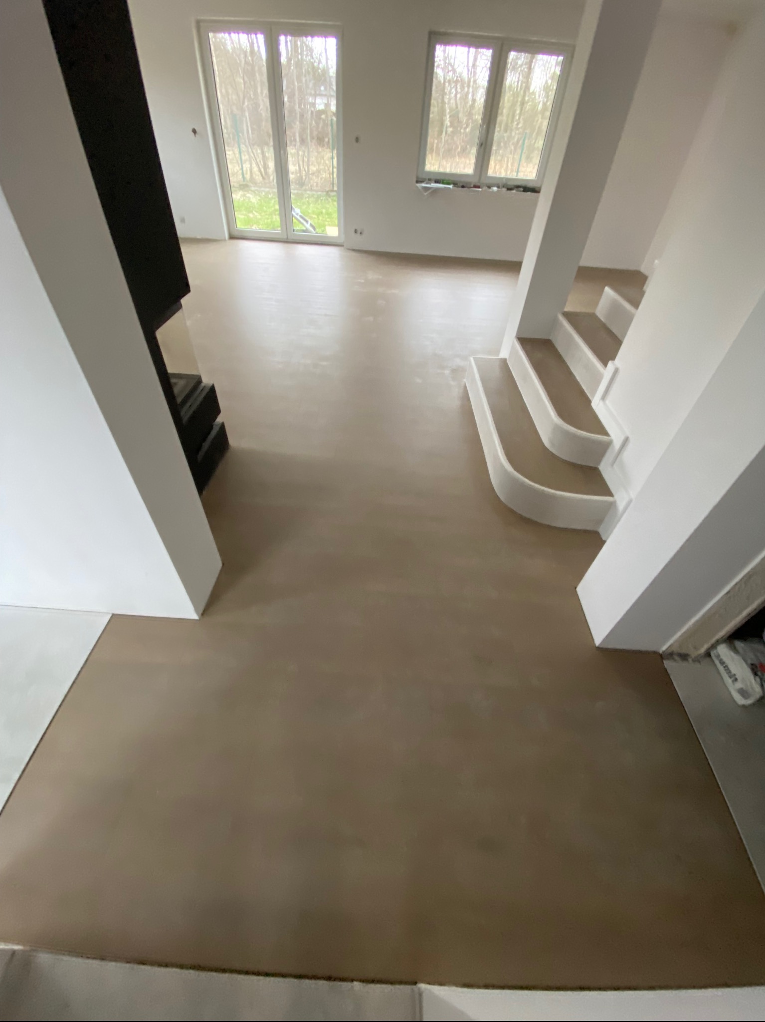 Nowa, jasna podłoga w odcieniach beżu w przestronnym wnętrzu z białymi ścianami, widoczne schody z zaokrąglonymi stopniami i fragment kominka.