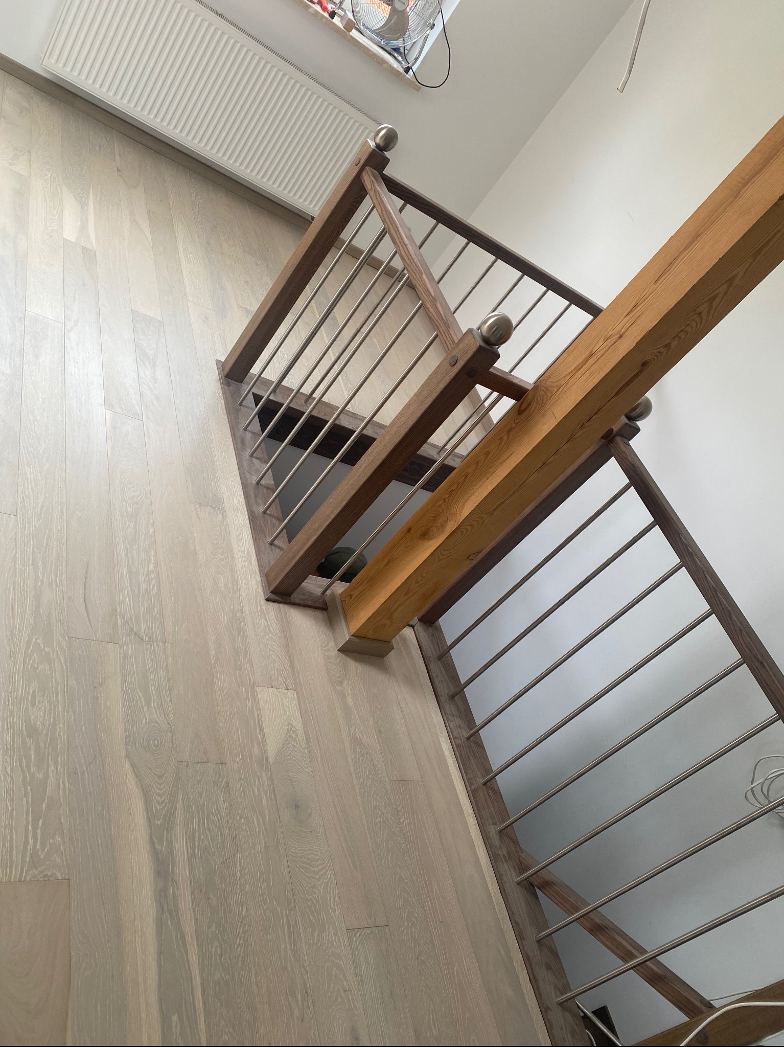 Jasna podłoga z desek i drewniane schody z metalowymi barierkami, widok z góry, oświetlenie dzienne. Minimalistyczny design z elementami naturalnego drewna.