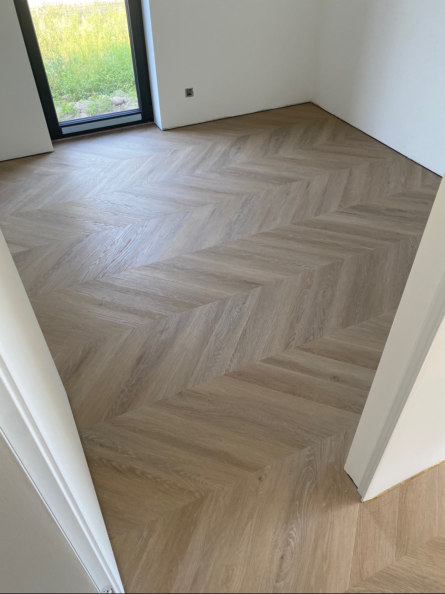 Jasna podłoga ułożona w jodełkę francuską w nowym wnętrzu z oknem i białymi ścianami. Widok z góry, naturalne światło.