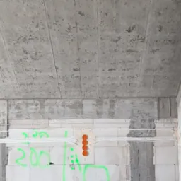 Surowy stan budynku w trakcie prac elektrycznych: widoczne kable w białych peszlach prowadzone wzdłuż ściany z betonu komórkowego, pomarańczowe puszki instalacyjne, betonowy strop ze śladami...