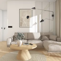 Jasne wnętrze salonu z beżową sofą narożną, okrągłym stolikiem kawowym z wazonem i książkami, abstrakcyjnym obrazem na ścianie oraz lampą sufitową w stylu industrialnym.