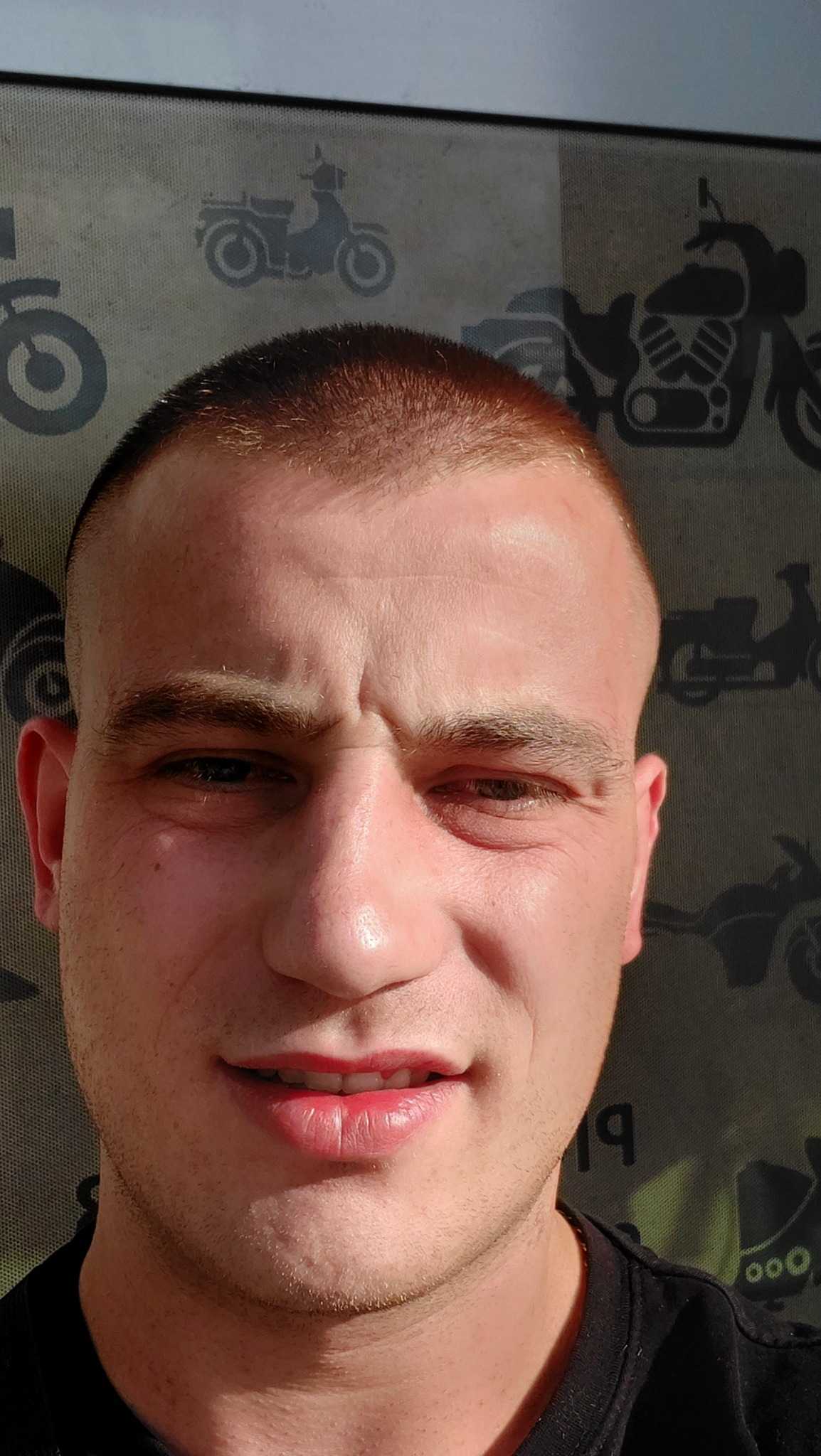 Portret mężczyzny z krótkimi włosami na tle ściany z motywem motocykli.