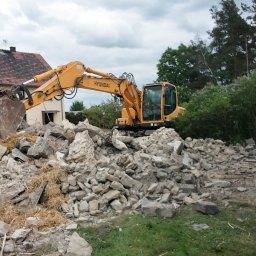 Usługi remontowo wykonczeniowe - Żółta koparka Hyundai na gruzowisku po rozbiórce w Strzelcach Opolskich. Widoczny fragment budynku i drzewa w tle. Prace wyburzeniowe w toku.