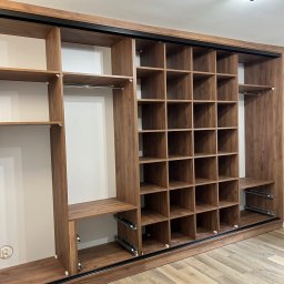 Meble na wymiar - Kalwaria Zebrzydowska - Wnętrze brązowej szafy przesuwnej z półkami i drążkami, widoczne prowadnice szuflad, na podłodze panele imitujące drewno.