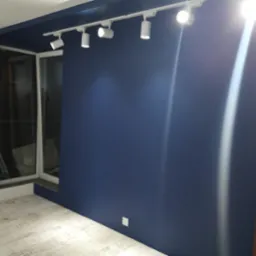 Pomieszczenie po malowaniu na ciemny niebieski kolor z zamontowanym oświetleniem szynowym, widoczne okno i fragment drzwi.