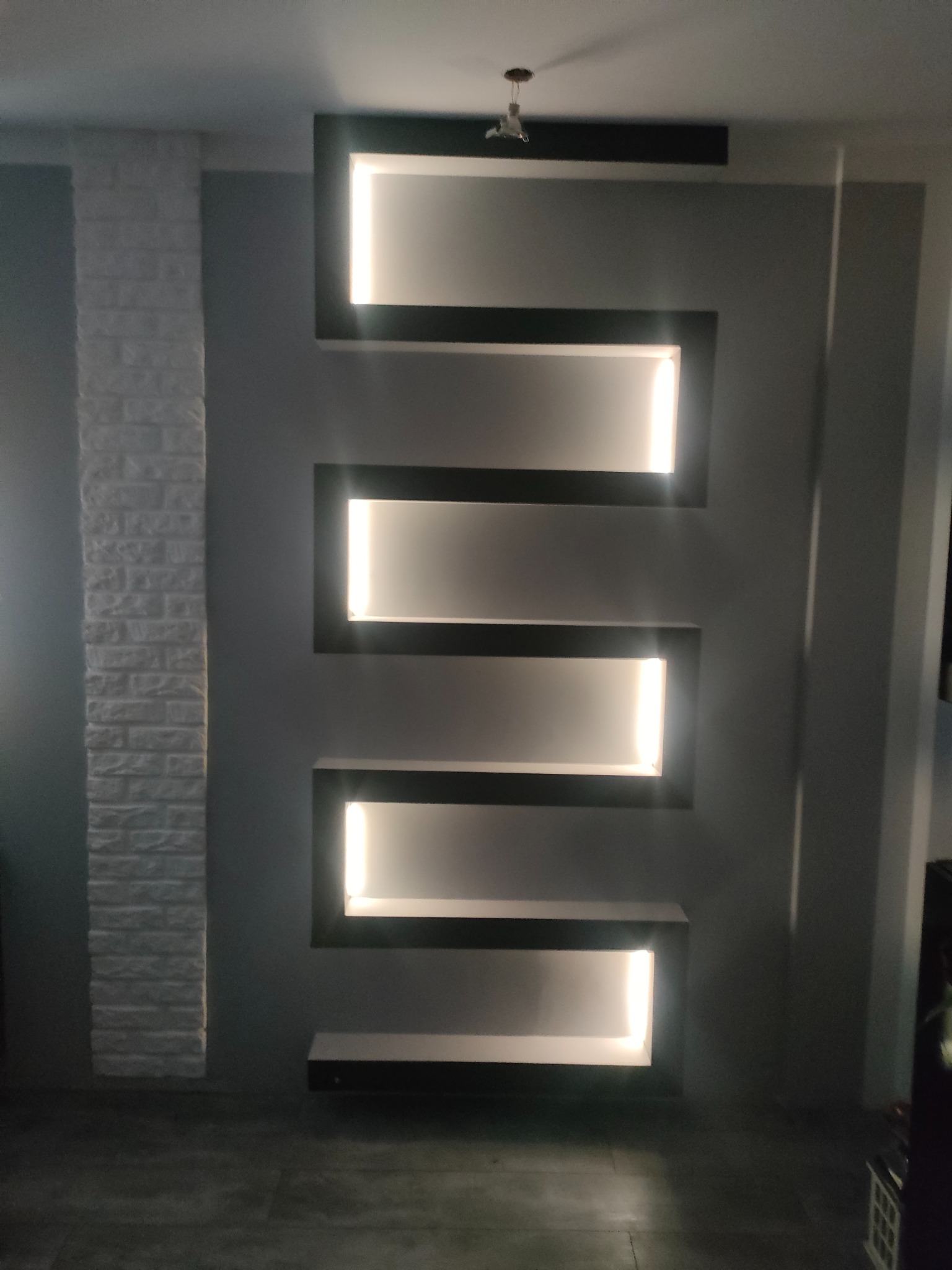 Ściana z dekoracyjnymi, podświetlanymi wnękami w kształcie litery Z, obok pionowy fragment ściany imitujący białą cegłę.