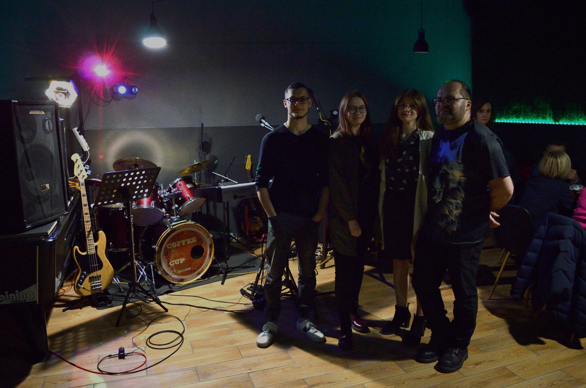 Zespół muzyczny Coffee Cup na scenie z perkusją z napisem, basem, klawiszami, nagłośnieniem i oświetleniem, pozujący z publicznością.