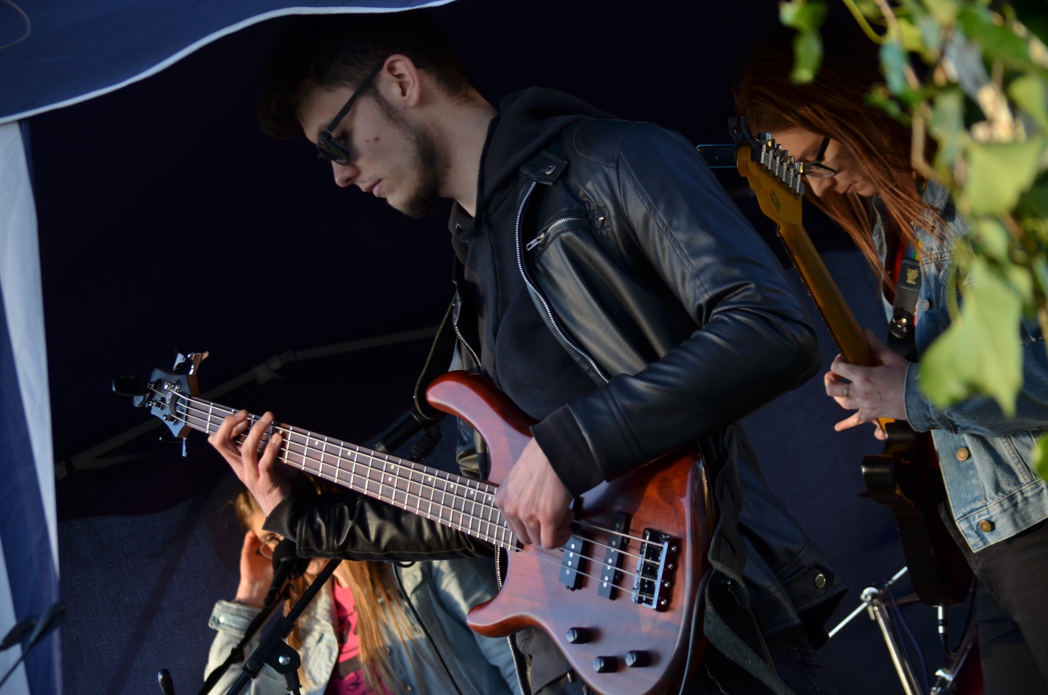 Muzycy grający na basie i gitarze elektrycznej pod namiotem, z widocznymi mikrofonami i fragmentami instrumentów innych muzyków.
