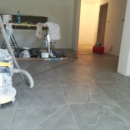 KOMPLEX-DOM Robert Łach - Wnętrze w trakcie remontu: szary gres na podłodze, drabina z narzędziami, odkurzacz przemysłowy i ściany przygotowane do malowania.