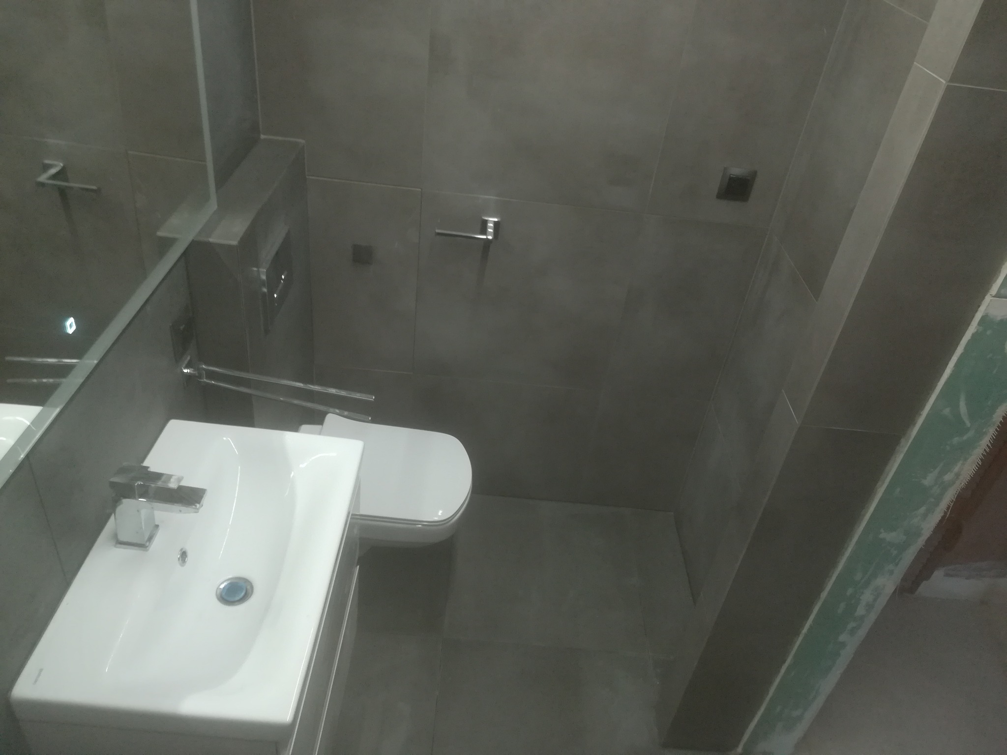 Nowoczesna łazienka z szarymi płytkami, białą umywalką nablatową i toaletą, widok z góry, oświetlenie punktowe.