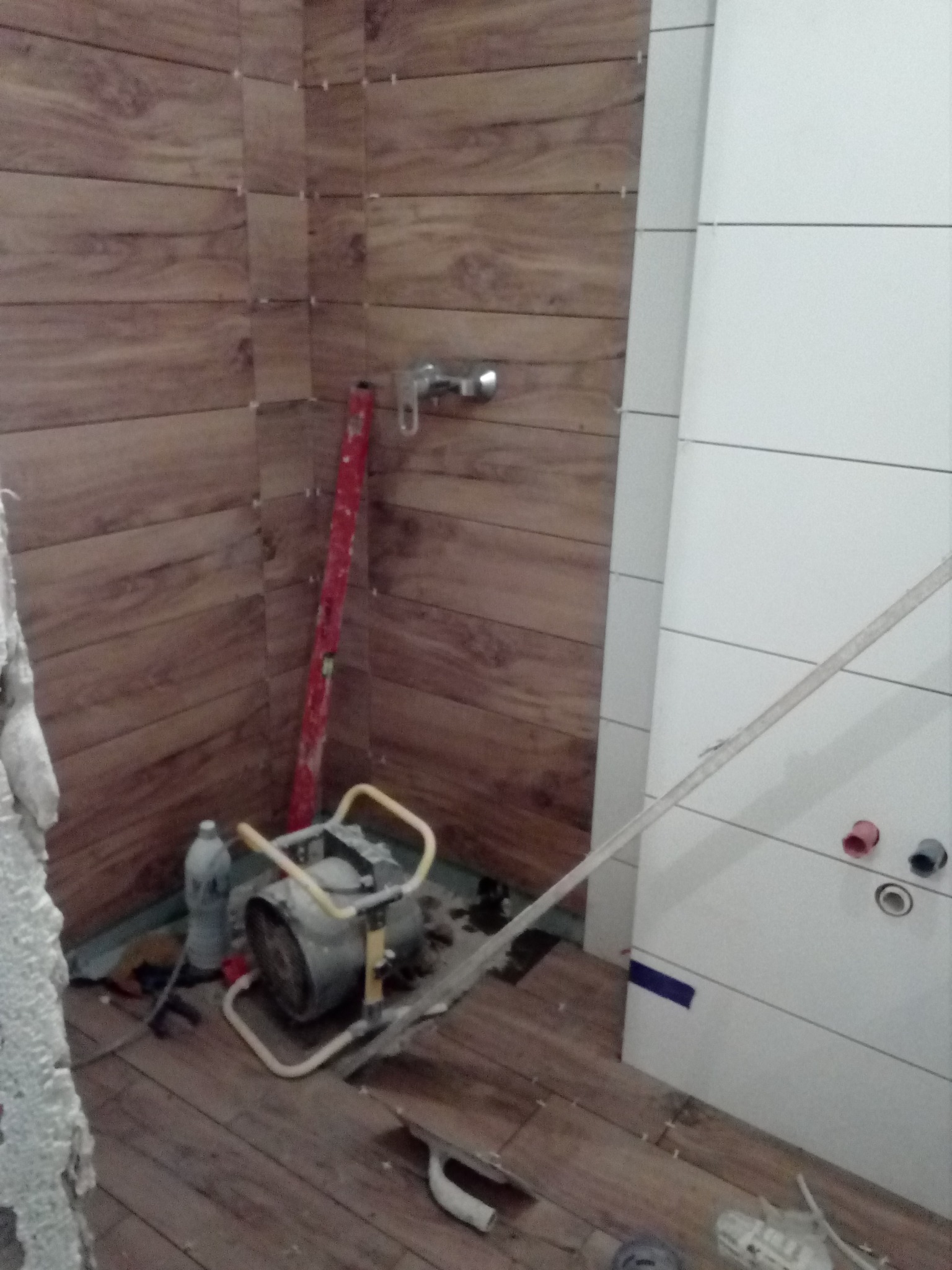 Układanie płytek imitujących drewno na ścianach i podłodze łazienki w trakcie prac wykończeniowych, widoczna poziomica, grzejnik i narzędzia.