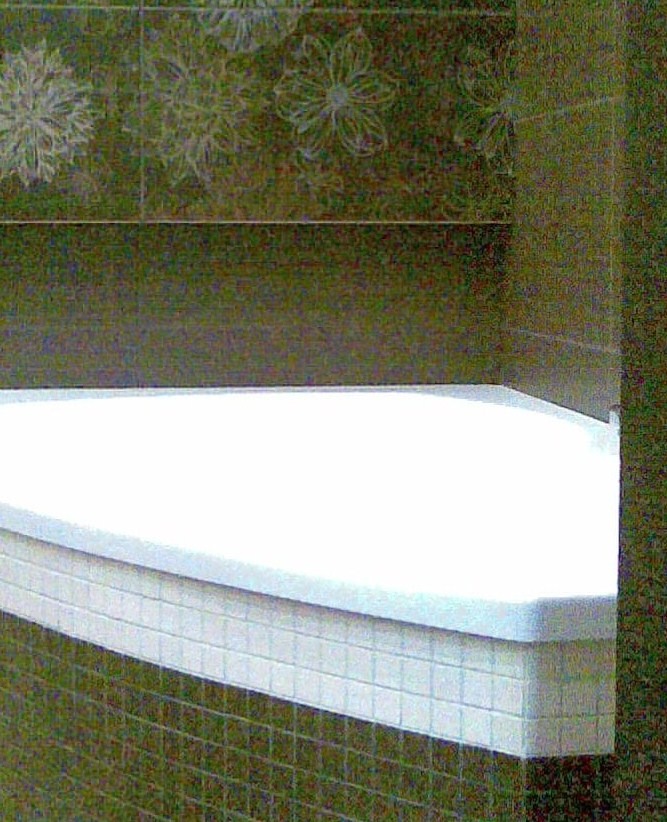 Biała, półokrągła wanna obudowana mozaiką na tle ciemnozielonych płytek z motywem kwiatowym.