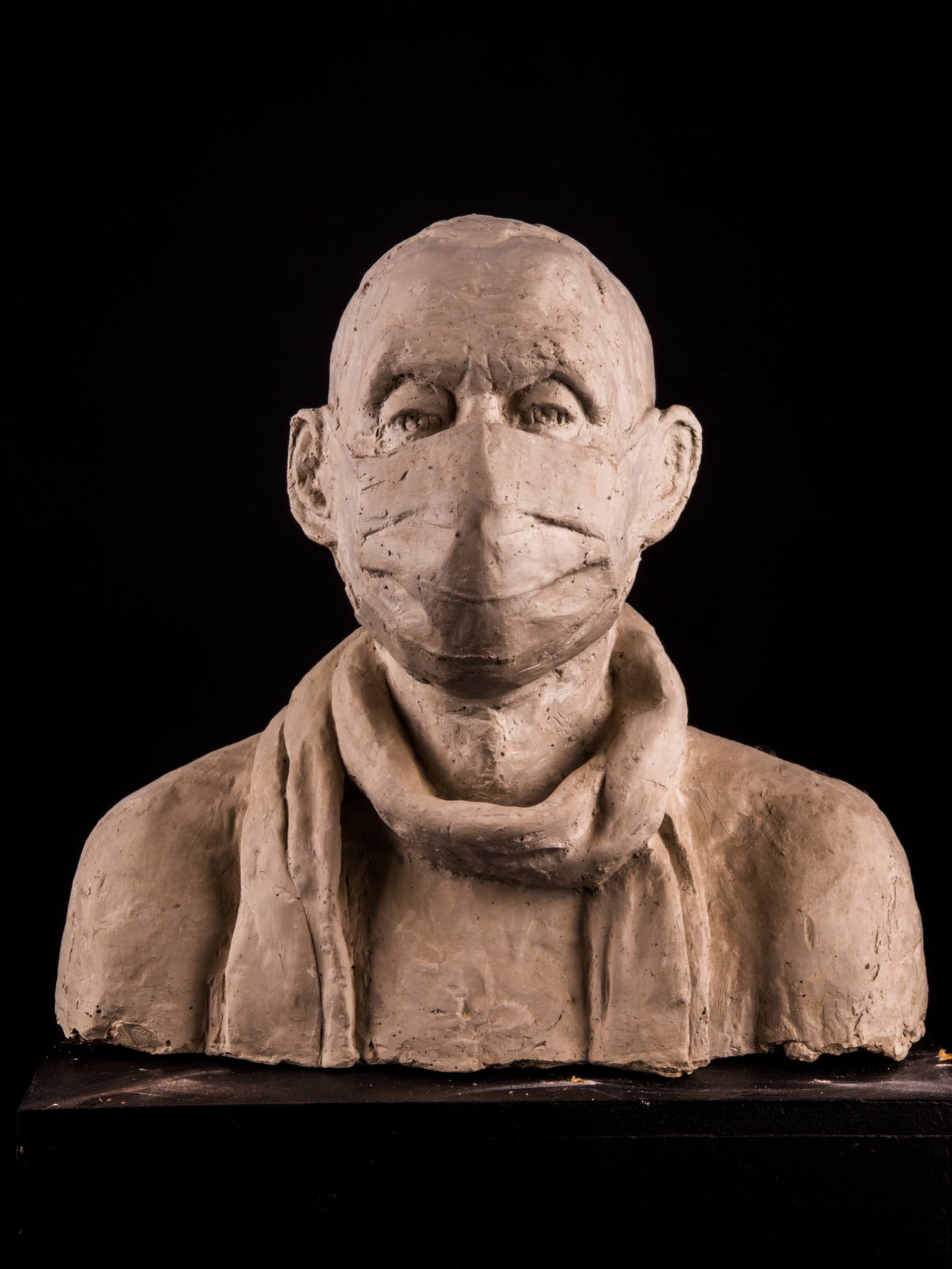 Gipsowe popiersie mężczyzny z maską na twarzy i szalem na czarnym tle.