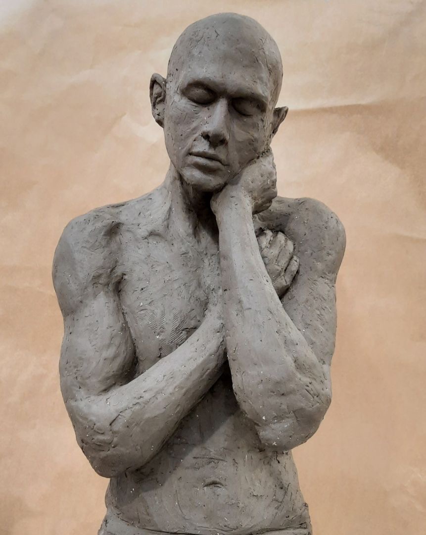 Gipsowa rzeźba torsu mężczyzny z zamkniętymi oczami, opierającego głowę na dłoniach na beżowym tle.