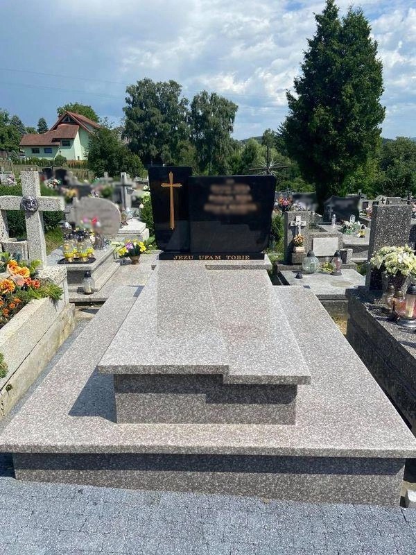 Granitowy pomnik z czarną tablicą i złotym krzyżem na cmentarzu, z napisem 'Jezu ufam Tobie'.