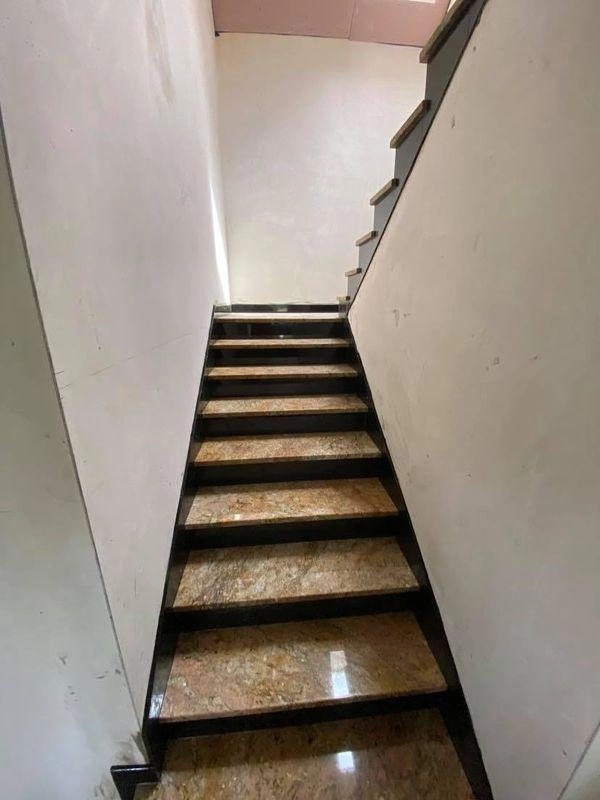 Wewnętrzne schody z okładziną w odcieniach beżu i brązu, czarne poręcze, widok od dołu.