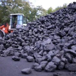 Góra czarnego węgla kamiennego na placu składowym, z ładowarką kołową w tle, częściowo zasłoniętą przez hałdę.