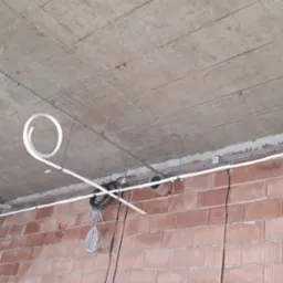 Montaż instalacji wentylacyjnej: białe rury prowadzone pod betonowym sufitem, mocowane do metalowych szyn na tle ściany z czerwonej cegły.