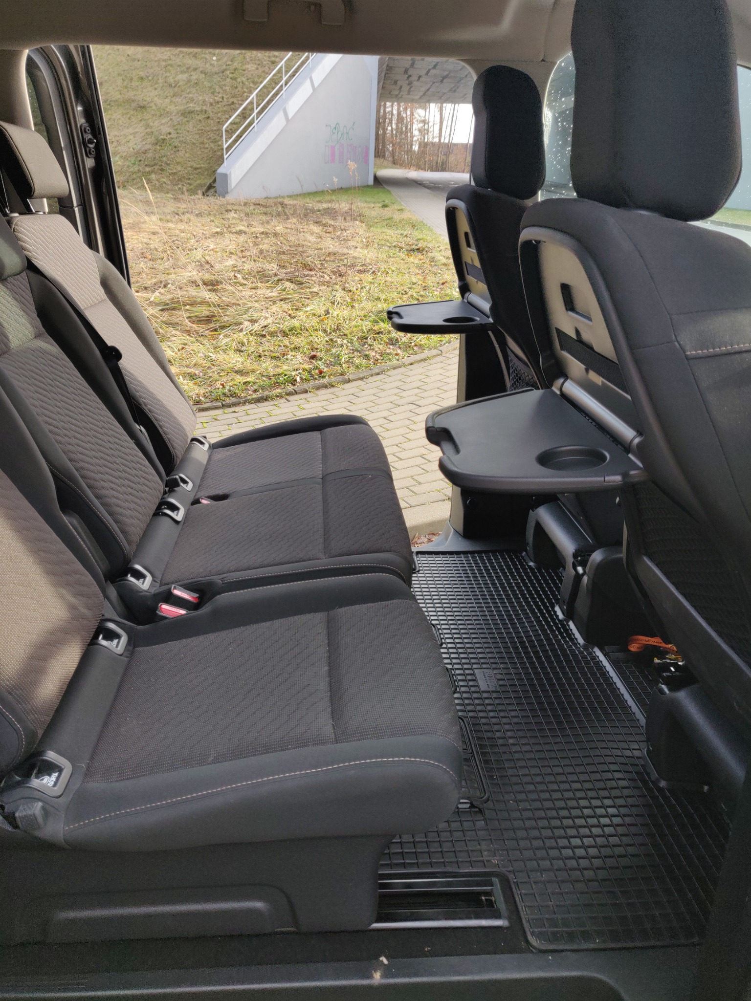 Wnętrze samochodu z trzema rzędami siedzeń, rozkładanymi stolikami przy tylnych siedzeniach i gumową wycieraczką na podłodze.