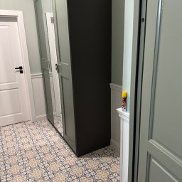 Budprint sp. z o.o. - Nowoczesne wykończenie wnętrza: szafa z lustrami, wzorzysta podłoga i białe drzwi w pastelowej kolorystyce. Widoczna listwa przypodłogowa i ściana w jasnym odcieniu.