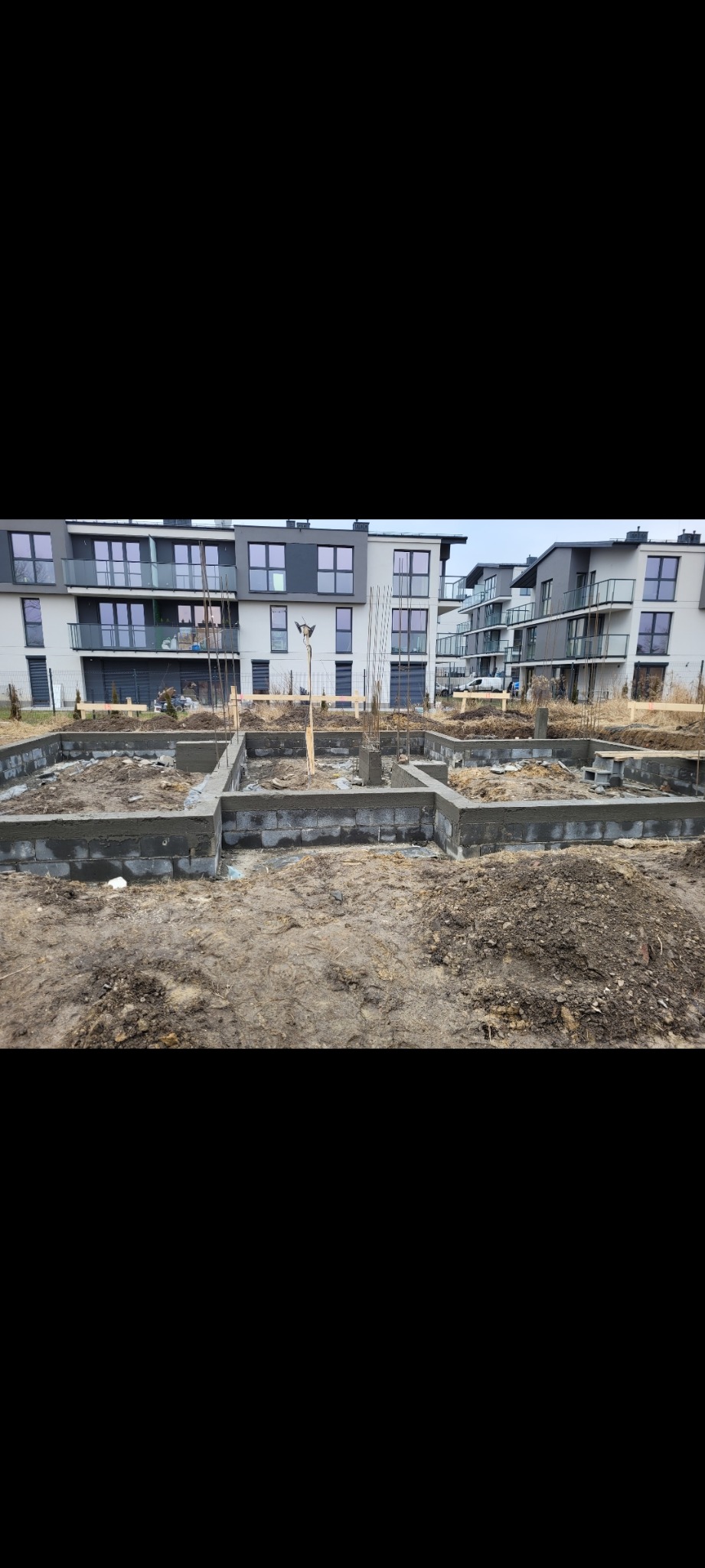 Wylane fundamenty budynku wielorodzinnego z widocznymi zbrojeniami i bloczkami betonowymi, na tle nowoczesnej architektury.