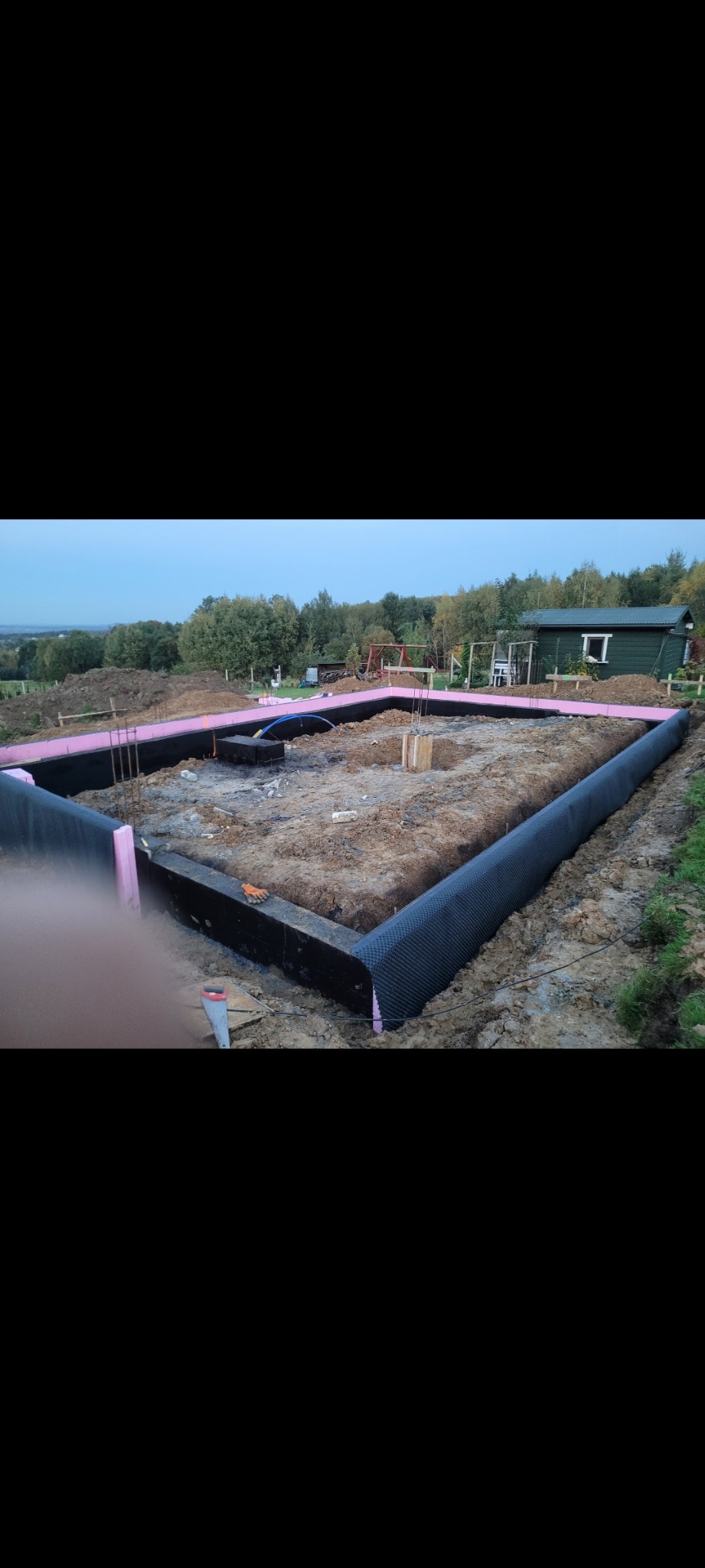 Przygotowany teren pod budowę domu z izolacją przeciwwilgociową i termiczną fundamentów, widoczne zbrojenie i elementy szalunkowe.