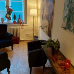 Przytulny pokój z dwoma fotelami klubowymi, drewnianą podłogą, oknem z dekoracjami świątecznymi, obrazami na ścianie i lampami