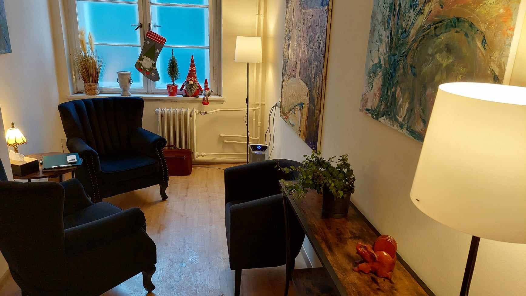 Przytulny pokój z dwoma fotelami klubowymi, drewnianą podłogą, oknem z dekoracjami świątecznymi, obrazami na ścianie i lampami