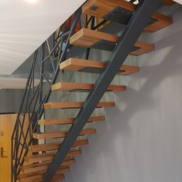 Ekoauto - Nowoczesne schody z drewnianymi stopniami i metalową konstrukcją nośną w kolorze grafitowym, z geometrycznym wzorem balustrady, zamontowane przy szarej ścianie w jasnym wnętrzu.