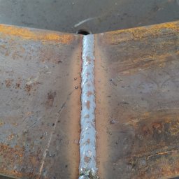 Ekoauto - Świeżo wykonane spoiny łączące dwie zardzewiałe, metalowe płyty, widoczne krople metalu i nierówności spoiny.