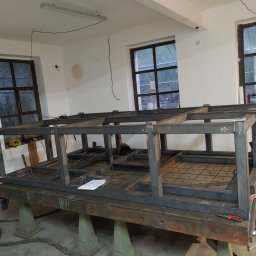 Ekoauto - Konstrukcja stalowa w trakcie spawania, widoczne okna w tle, leżące narzędzia i dokumentacja.