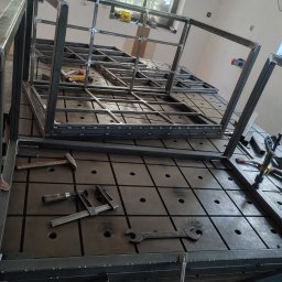 Ekoauto - Konstrukcja metalowa w trakcie spawania w Nowiźnie, widoczne narzędzia ślusarskie na perforowanym stole spawalniczym.