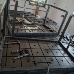 Konstrukcja metalowa w trakcie spawania w Nowiźnie, widoczne narzędzia ślusarskie na perforowanym stole spawalniczym.