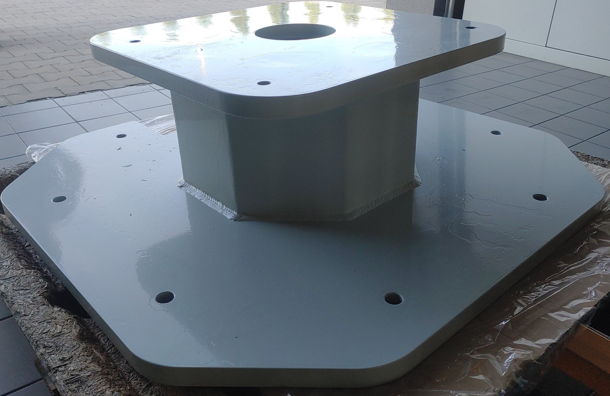 Szara, metalowa konstrukcja wspornikowa z widocznymi spawami i otworami montażowymi, leżąca na folii ochronnej.