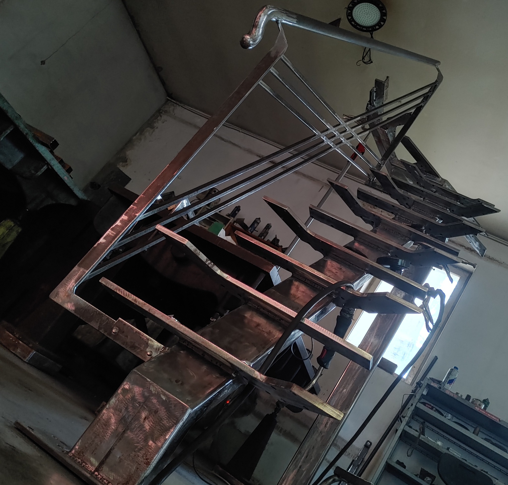 Szkielet metalowej konstrukcji schodów w trakcie spawania w warsztacie, widoczne elementy konstrukcyjne i spawarka.