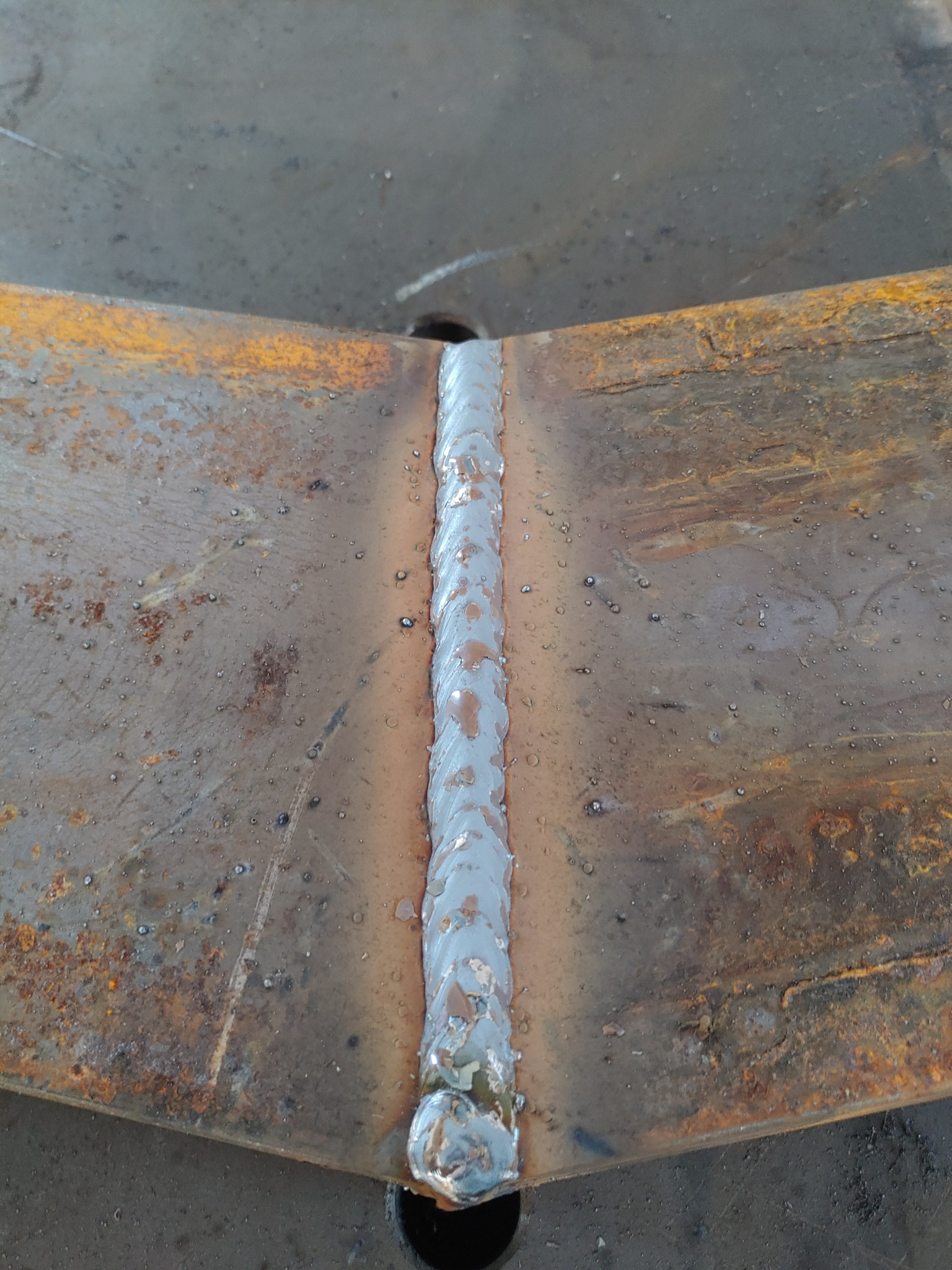 Świeżo wykonane spoiny łączące dwie zardzewiałe, metalowe płyty, widoczne krople metalu i nierówności spoiny.