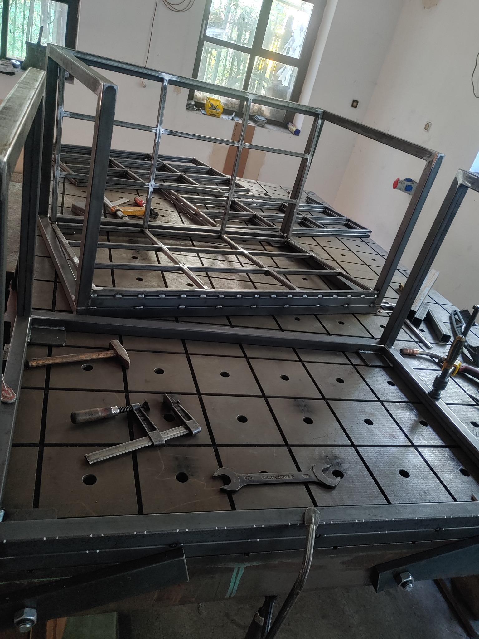 Konstrukcja metalowa w trakcie spawania w Nowiźnie, widoczne narzędzia ślusarskie na perforowanym stole spawalniczym.