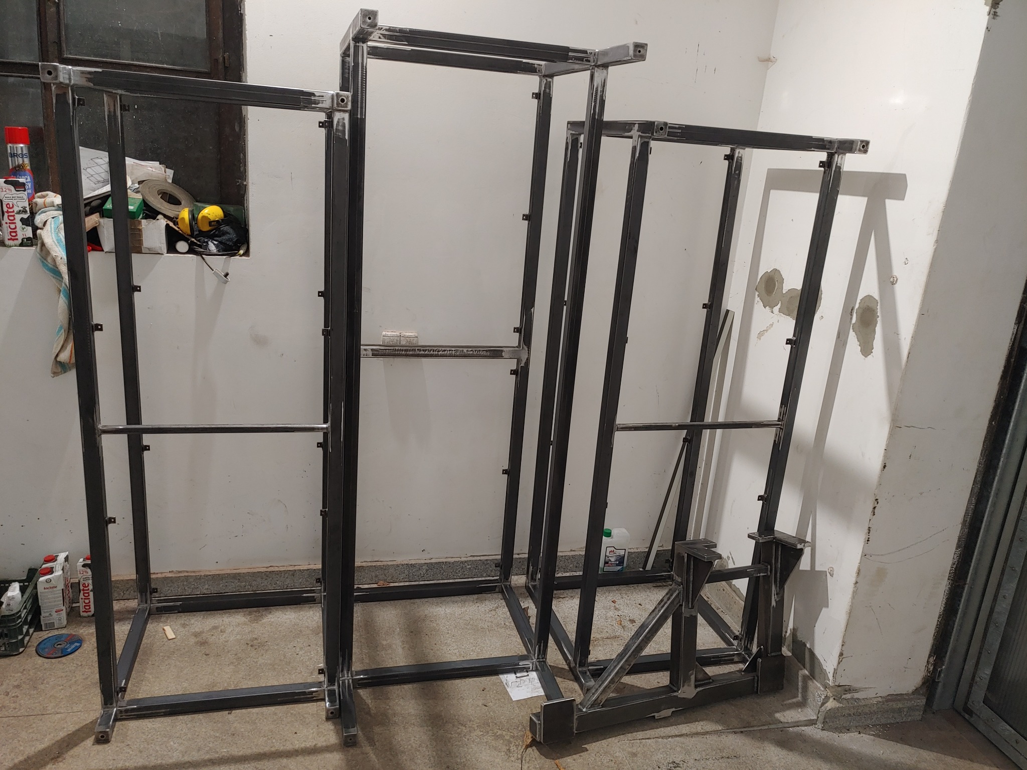 Trzy surowe, metalowe konstrukcje ramowe w warsztacie, z widocznymi śladami spawania i przygotowanymi otworami montażowymi, ustawione w różnej odległości od obiektywu, z narzędziami i materiałami...