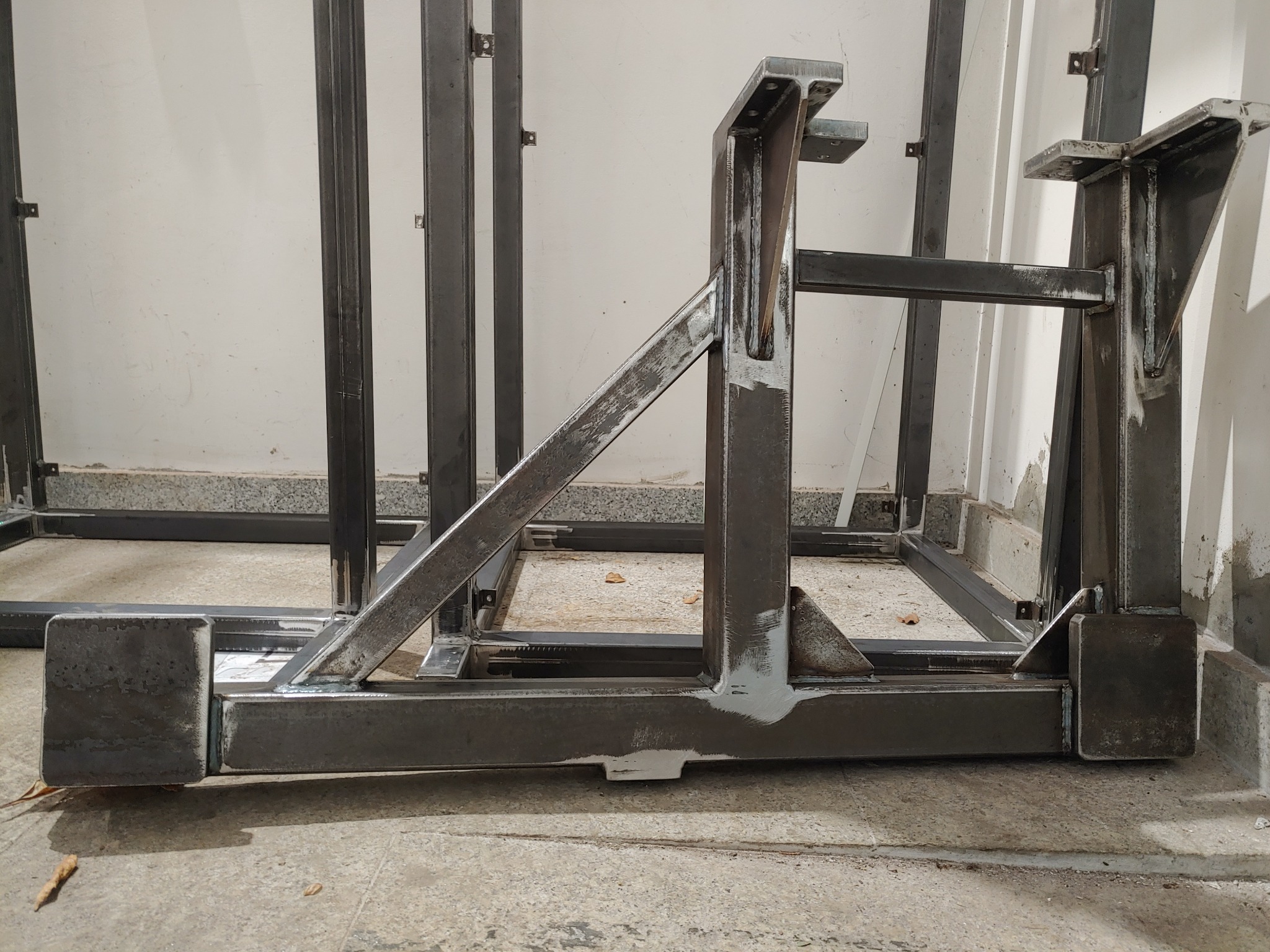 Surowa, spawana konstrukcja stalowa z profili, częściowo pomalowana farbą podkładową, widoczna na tle białej ściany, w trakcie budowy lub montażu.