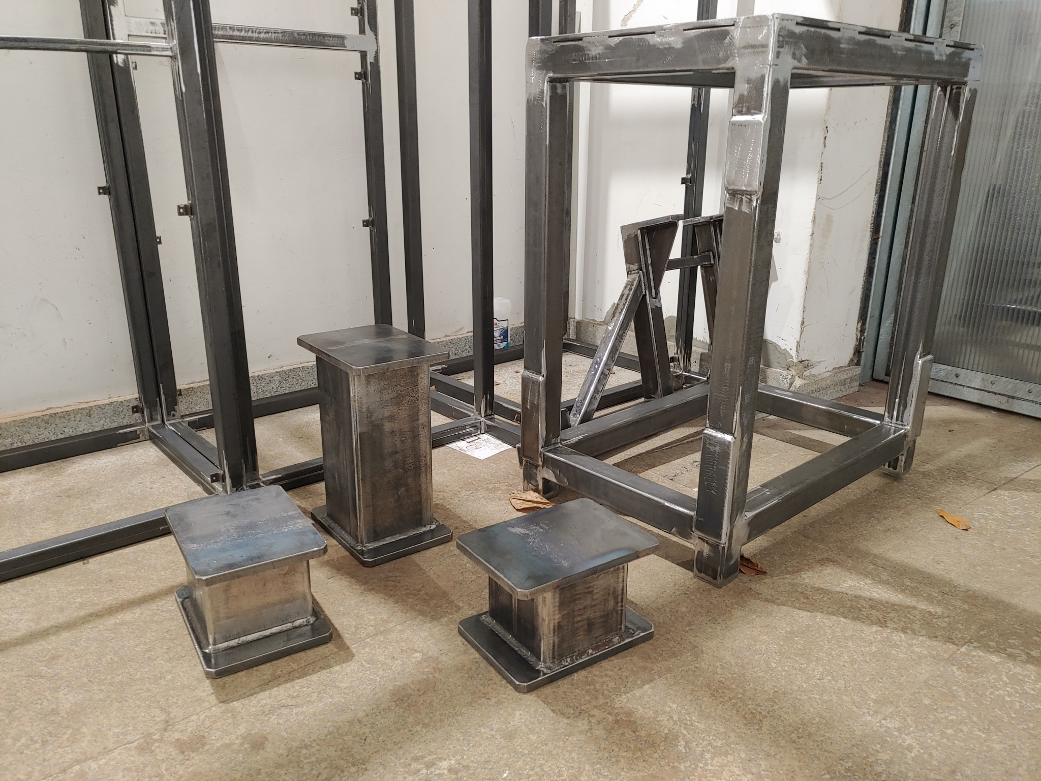 Surowe, spawane konstrukcje stalowe: rama, stoliki i podpory, w warsztacie, przed malowaniem lub wykończeniem.