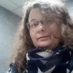 Portret kobiety w okularach i szalu w gwiazdy, na tle ściany z płytami.